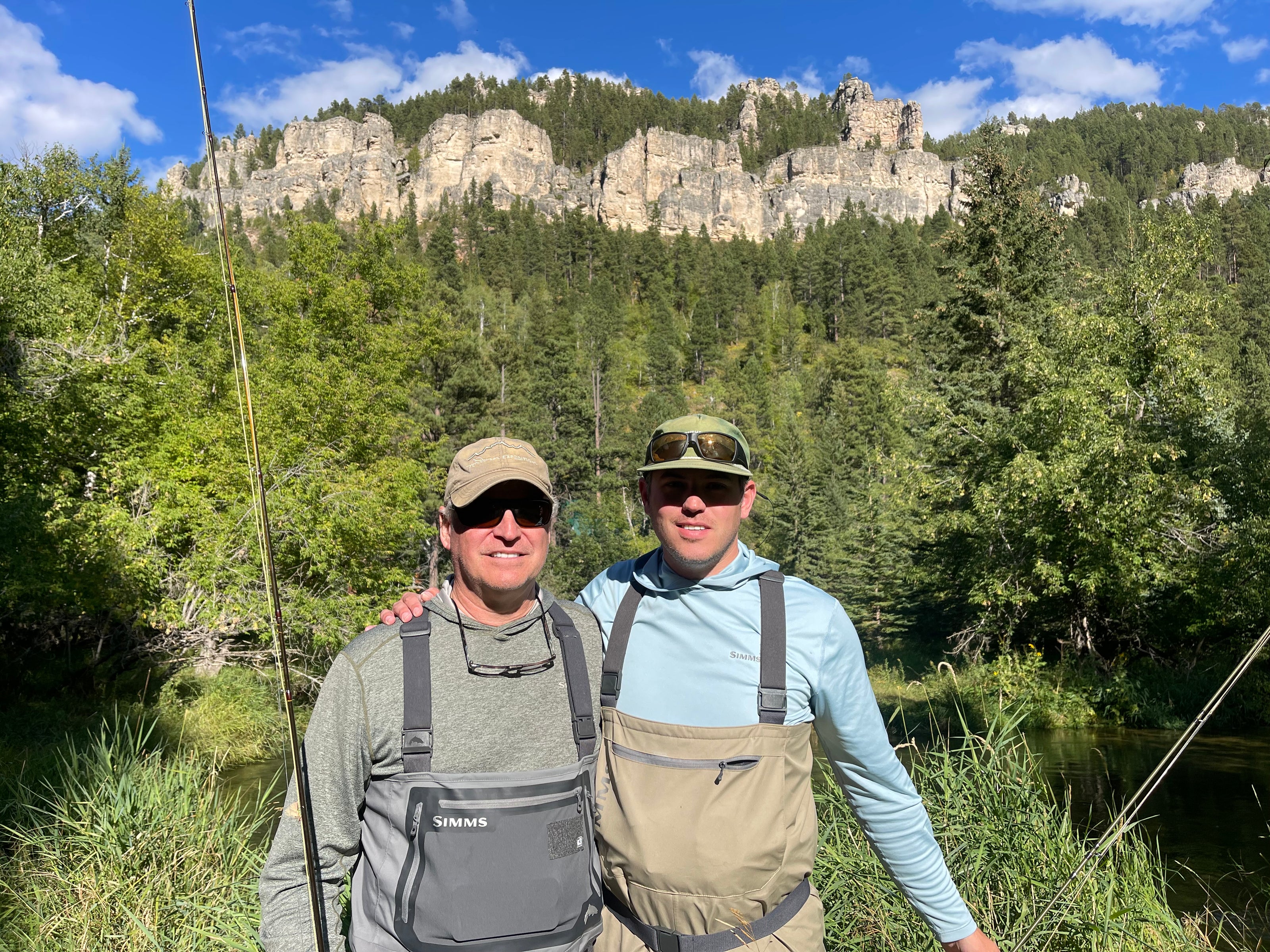 Image of two clients holding fishing rods next to a river