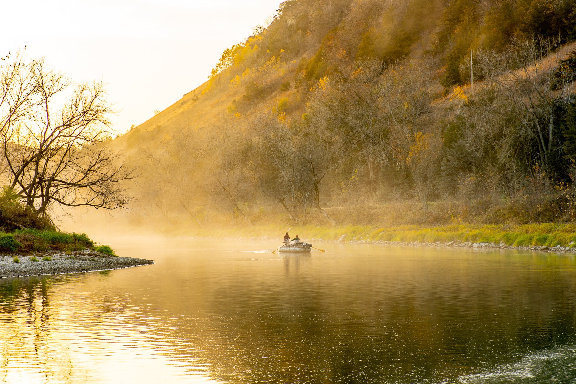 Image of a row boat in the distance on a river during a foggy dawn